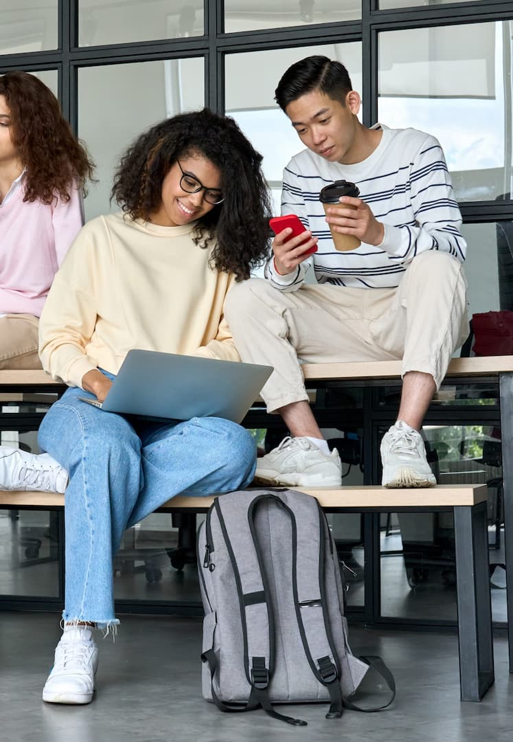 Étudiants multiraciaux au campus universitaire utilisant des appareils connectés.