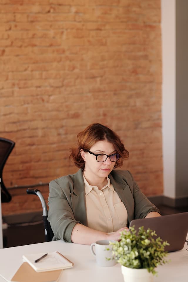Une femme en fauteuil roulant qui travaille sur un ordinateur portable derrière un bureau.