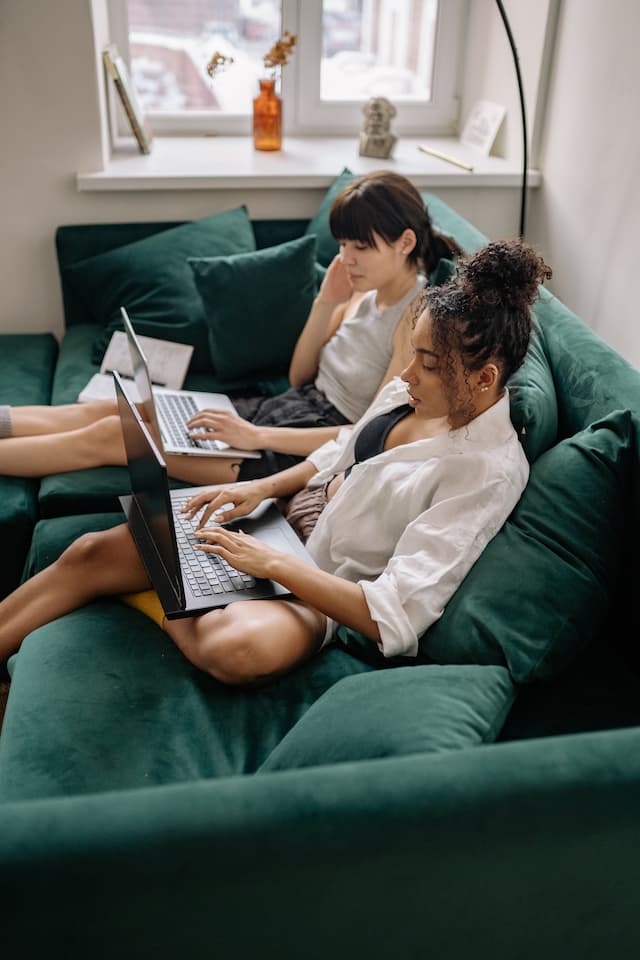 2 femmes qui travaillent sur leurs ordinateurs portables assises sur un canapé.
